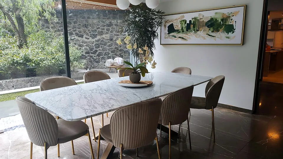 Comedor con cubierta de mármol y sillas tapizadas frente al jardín