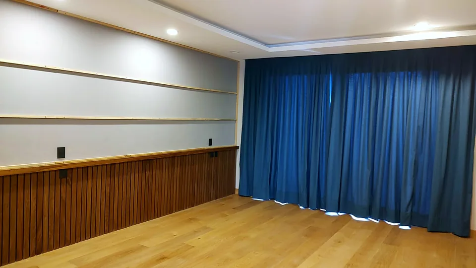 Recámara terminada con muro tapizado, lambrín de madera y cortinas azules