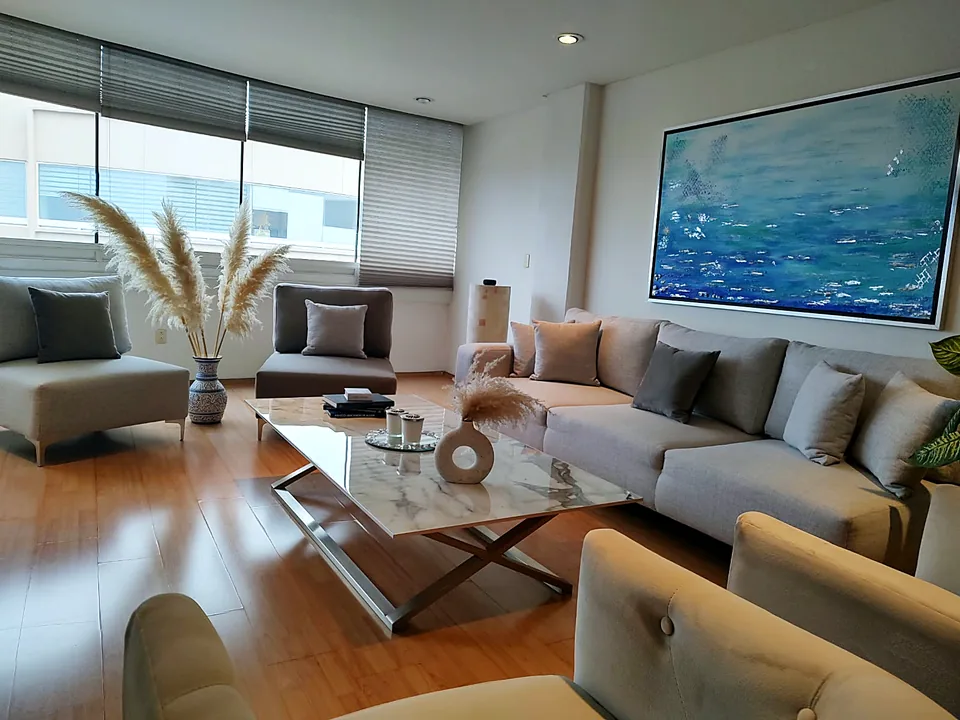 La misma sala después de la remodelación: sofá modular, mesa de mármol y cuadro azul