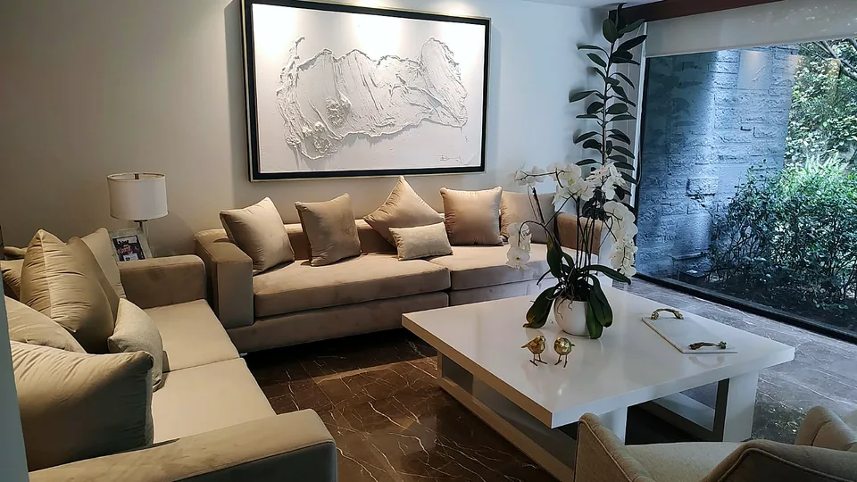 Sala en tonos arena con cuadro en relieve y ventanal al jardín