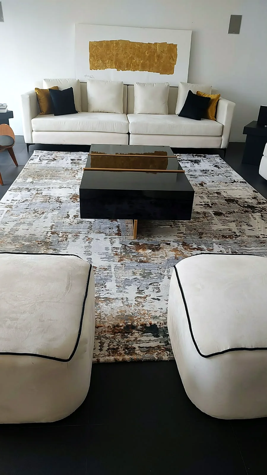 Sala blanca con cojines azul y dorado, mesa negra y otomanes tapizados