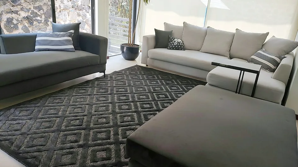 Sala modular gris con tapete geométrico frente a un muro de piedra