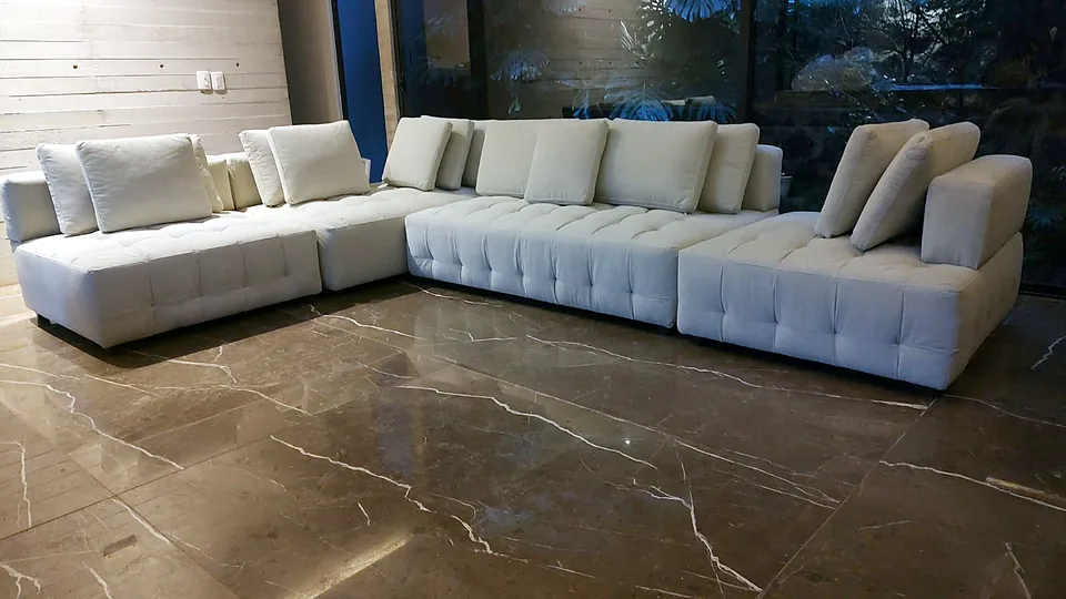 Sala seccional blanca capitonada sobre piso de mármol